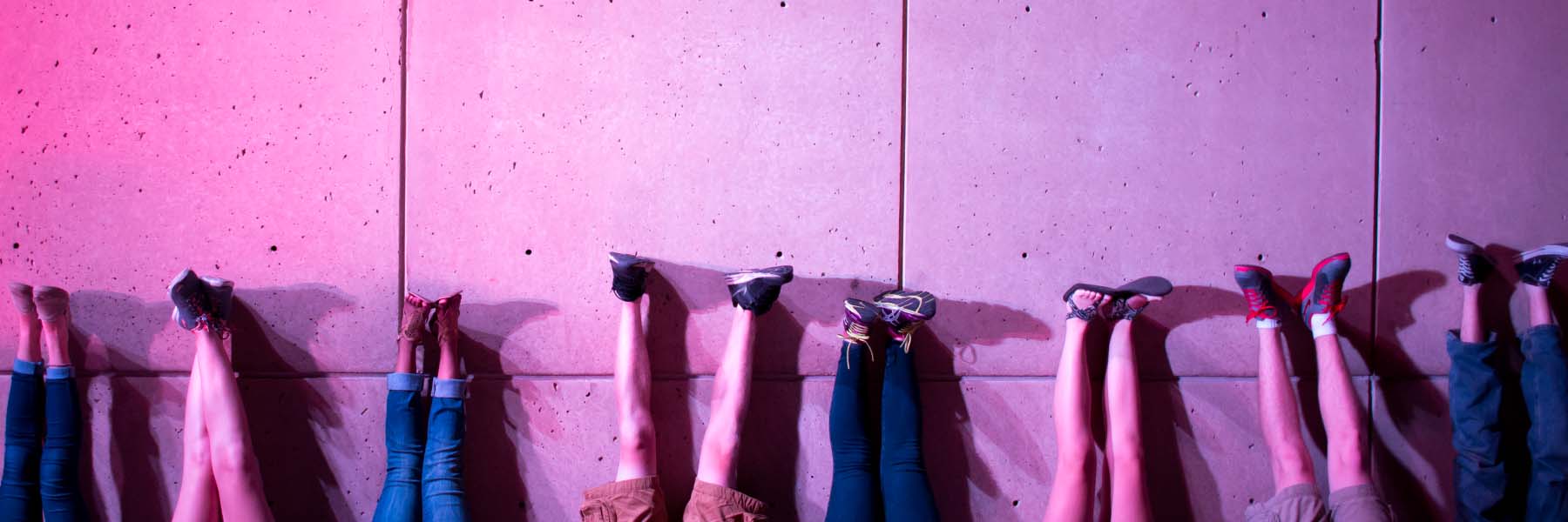 Students lie with their feet on the IU Art Museum wall in the pink glow of the light totem.